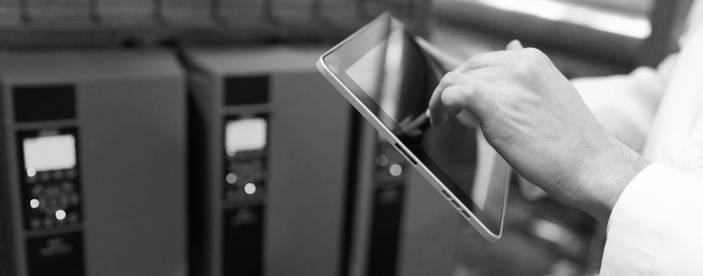 Portrait of man in a white robe and a cap standing in production department of dairy factory with grey tablet technologist with grey tablet in his hands make a set up of the production line while standing at the department of dairy factory
